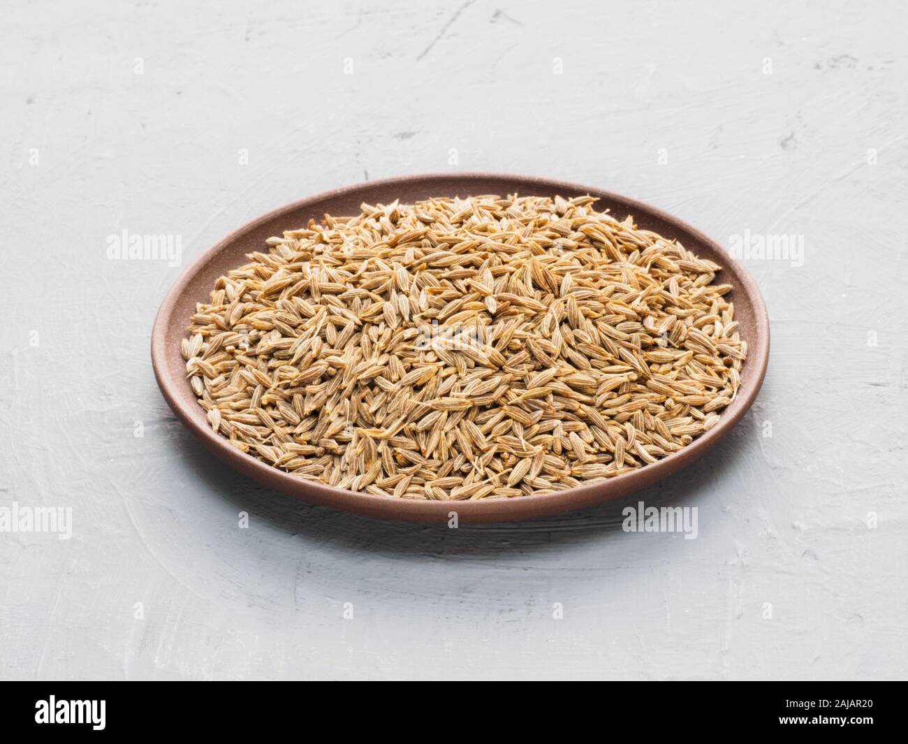 Spice cumin (jeera) in clay plate on gray concrete background. Diet and