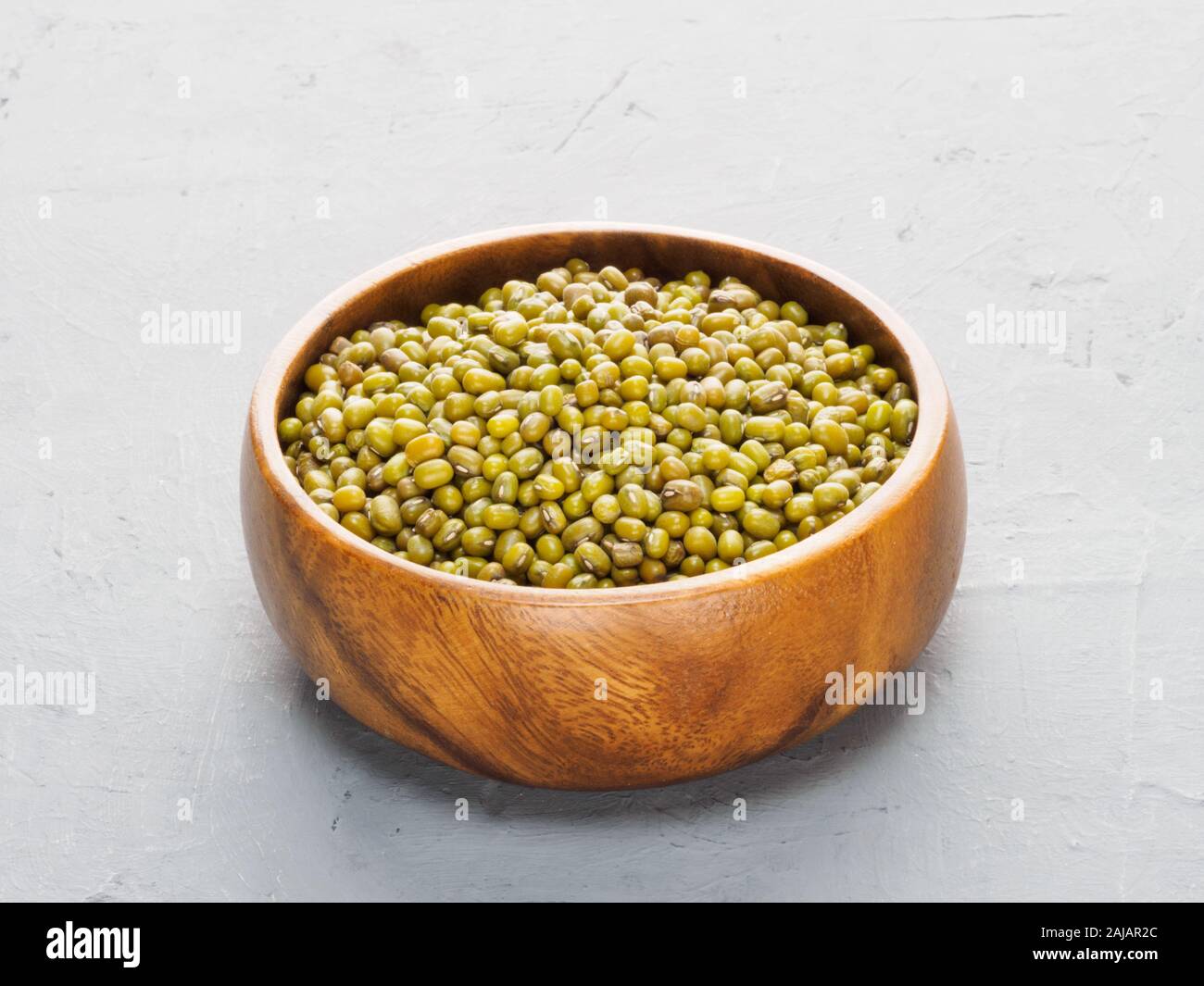 Green gram (bean) in wooden cup on gray concrete and beige fabric background. Healthy eating concept Stock Photo