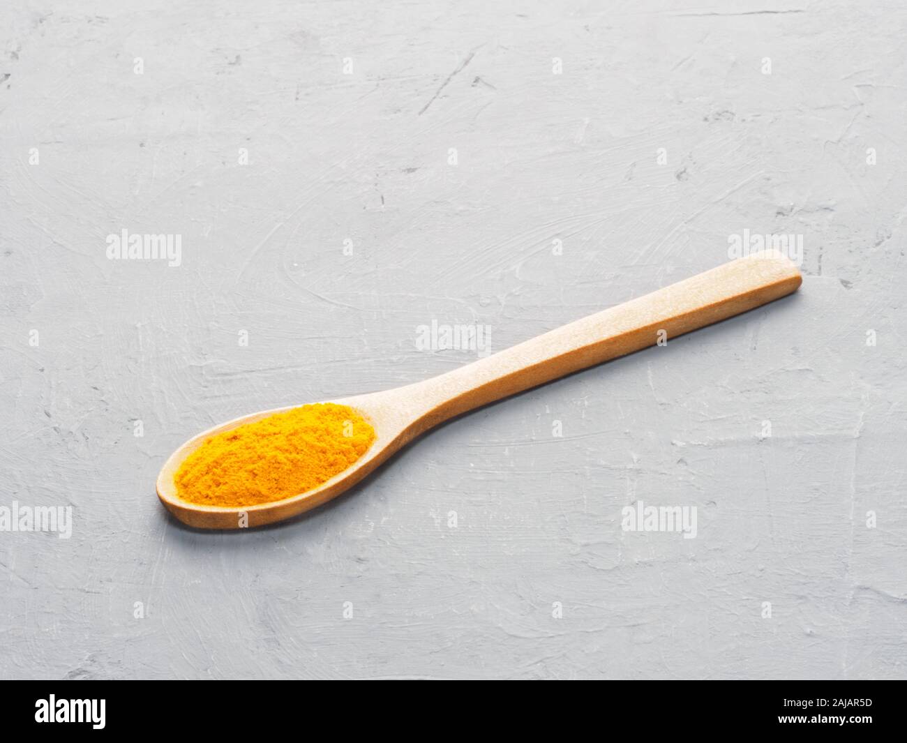 Spice turmeric in wooden spoon on gray concrete background. Indian cuisine, ayurveda, naturopathy concept Stock Photo