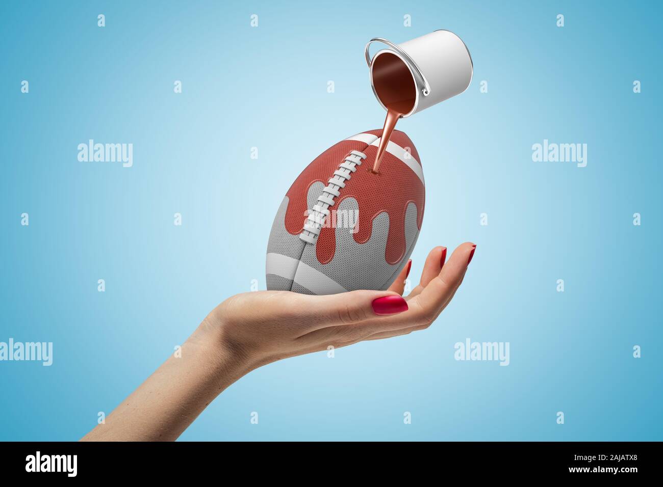 Female hand holding american football ball with small silver paint bucket turned upside down and brown paint pouring on it on blue background. Digital Stock Photo