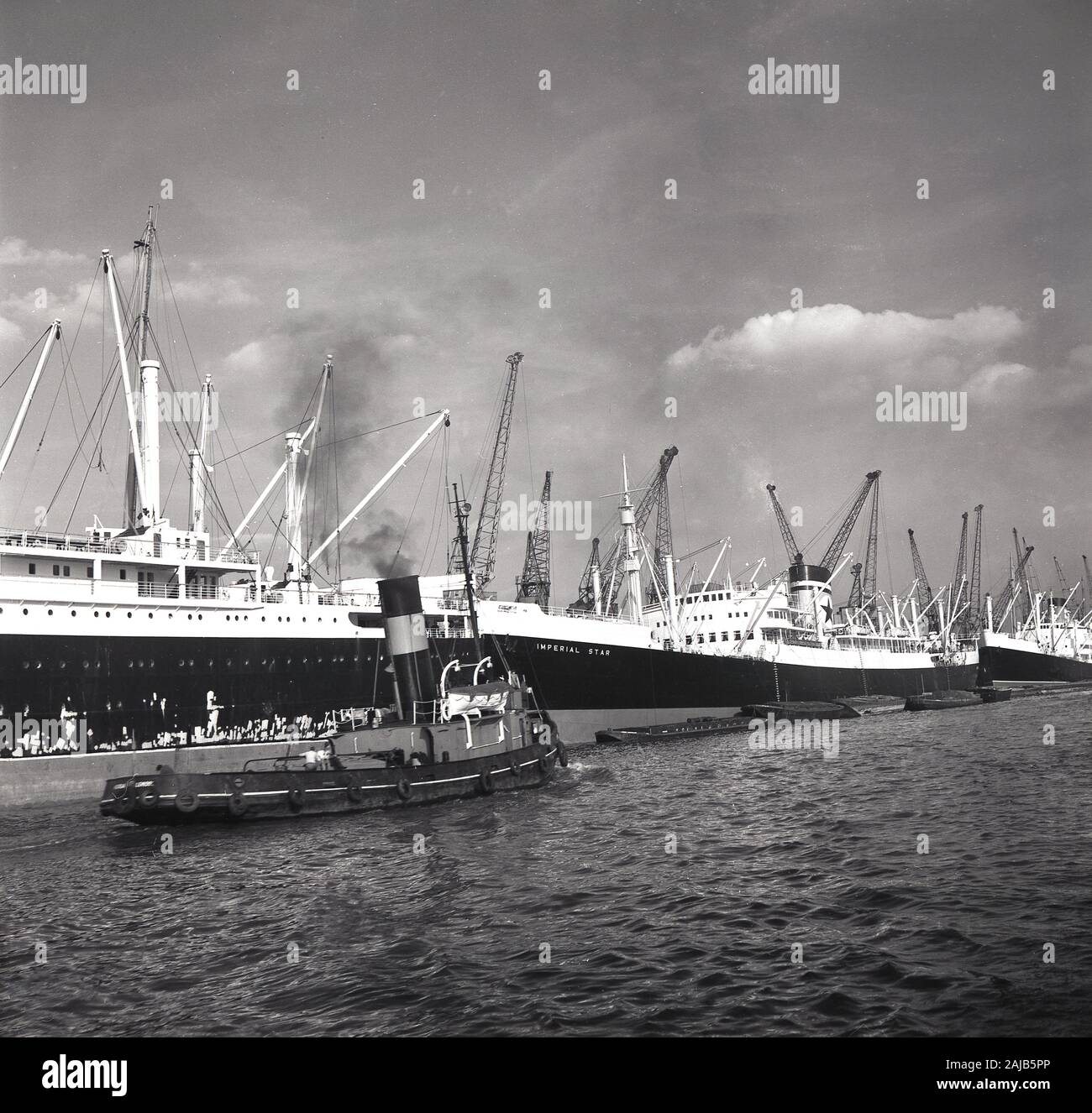 1960s, historical, three steamships moored up beside each other at a working London Docks, including the 'Imperial Star', a ship of the Blue Star line equipped with refrigerated machinery for the carriage of meat. The ship built in Belfast by Harland and Wolff, had 29 cargo spaces insulated by granulated cork. Blus Star line was founded by the Vestey Brothers, a Liverpool-based butchers company, who pioneered shipping refrigeration.  A steam drivern tugboat can also be seen going up the river. Stock Photo
