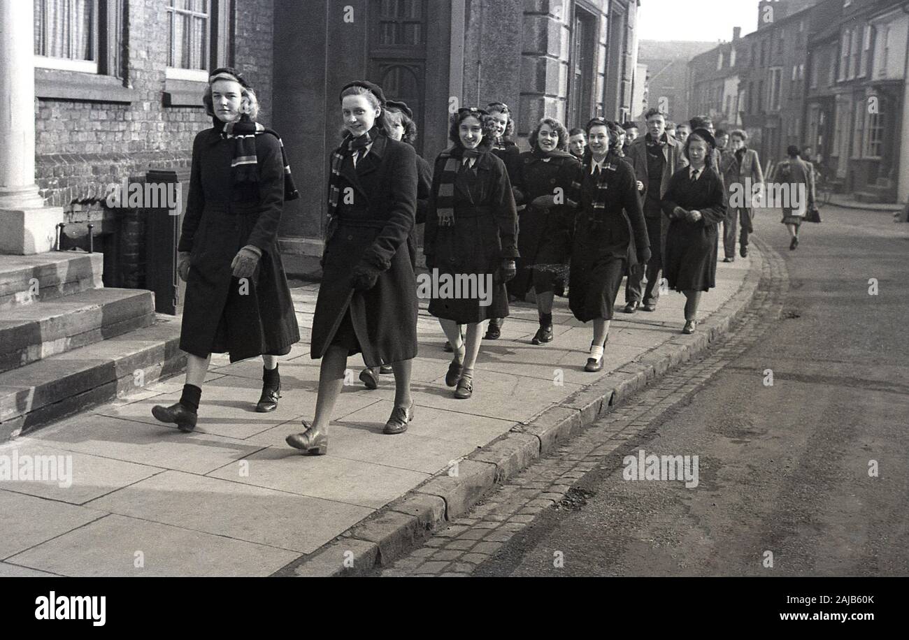 1950s, historical, uniformed schoolgirls and schoolboys in their school coats and scarfs walking along an English high street on their way to a church service, England, UK. Stock Photo