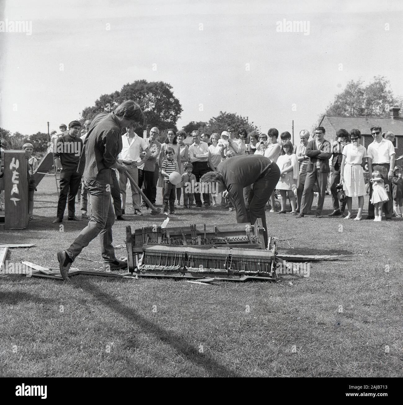 1960s, historical, piano smashing contest, at an English village fete, visitors watch two men using sledgehammers to destroy an upright piano into small pieces which could be passed through a 9-inch diameter hole. Such contests were popular at village fetes in the UK in the 1960s. Stock Photo