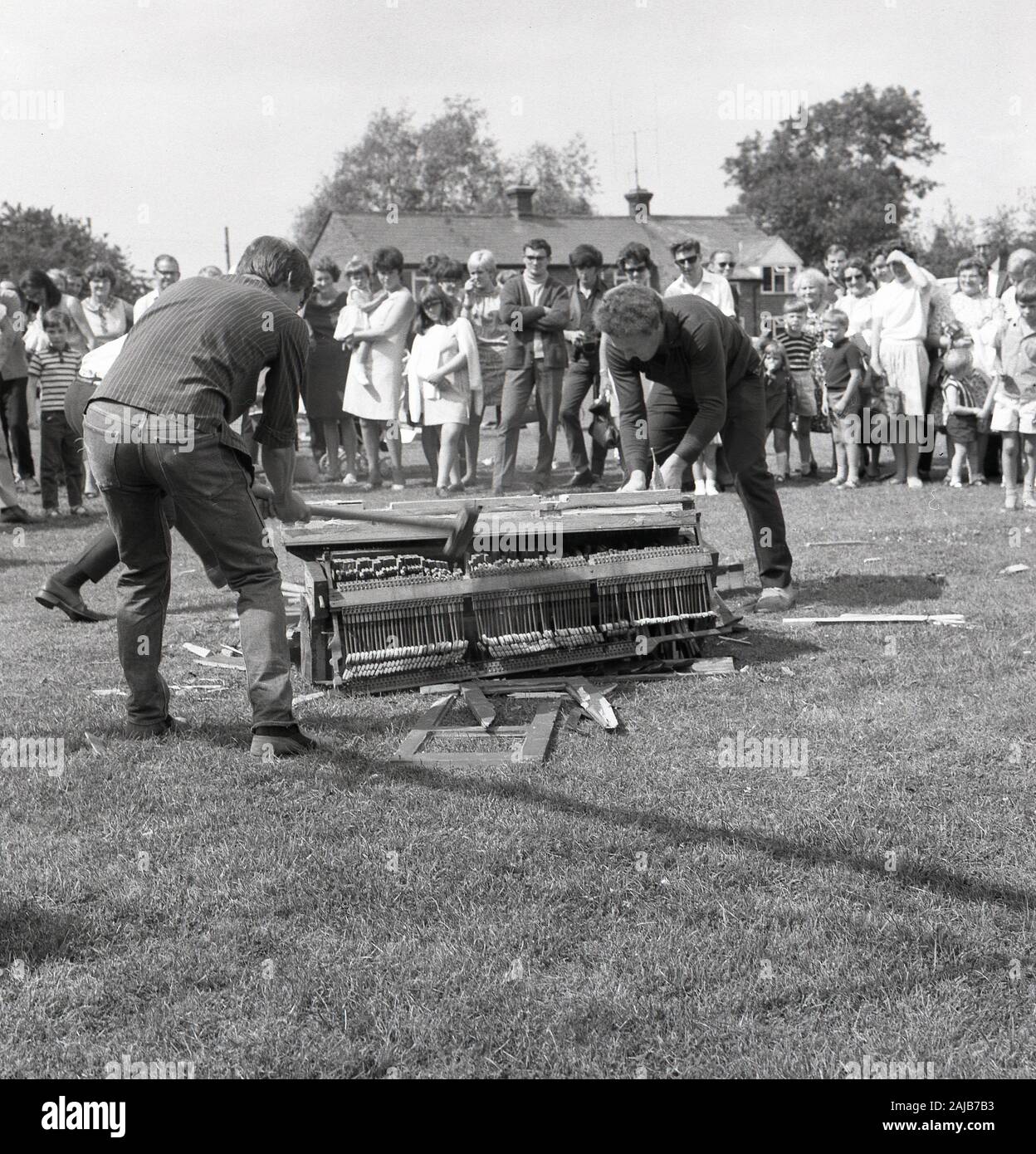 1960s, historical, piano smashing contest, at an English village fete, visitors watch two men using sledgehammers to destroy an upright piano into small pieces which could be passed through a 9-inch diameter hole. Such contests were popular at village fetes in the UK in the 1960s. Stock Photo