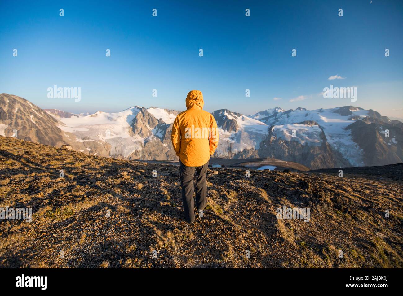 Rear view of hiker walking on mountain summit in yellow jacket. Stock Photo