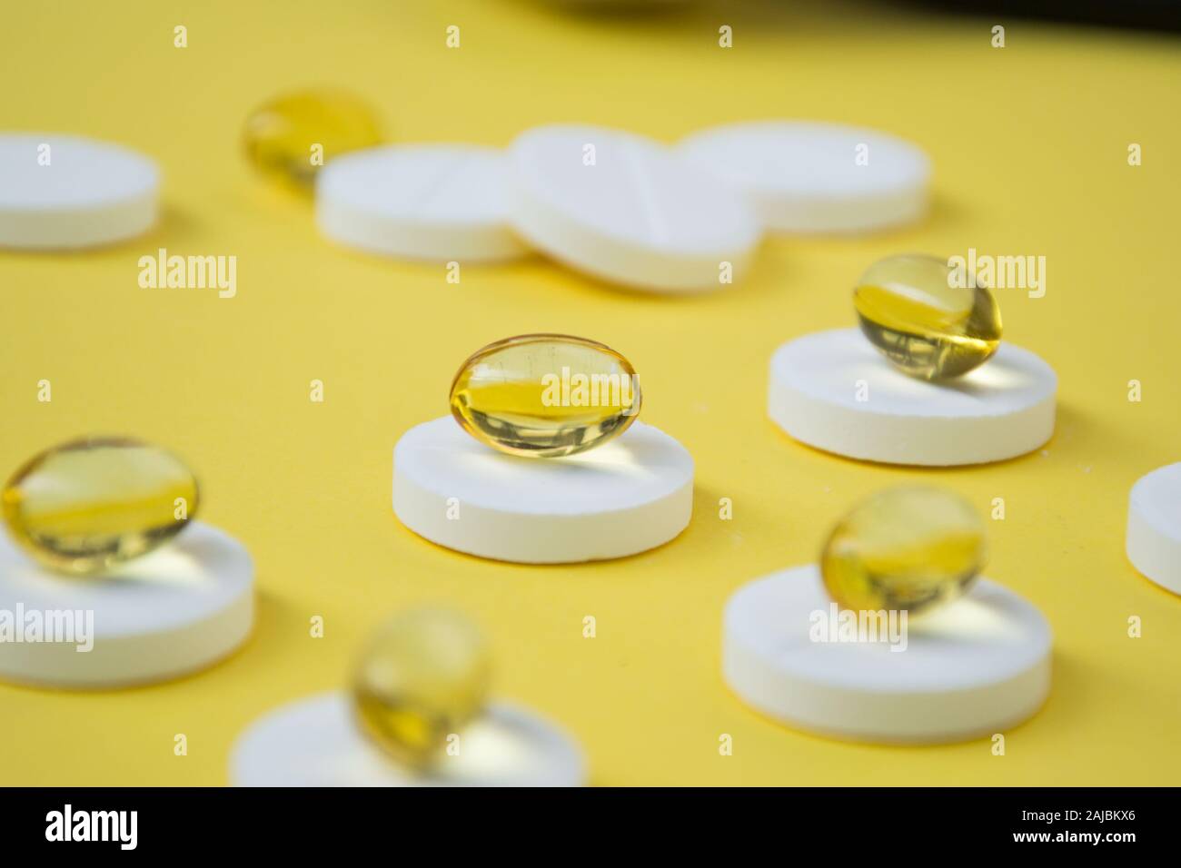 Close-up of golden colored oil supplements, soft gel capsule on top of round white pills, health concept, pharmaceutical tablets Stock Photo