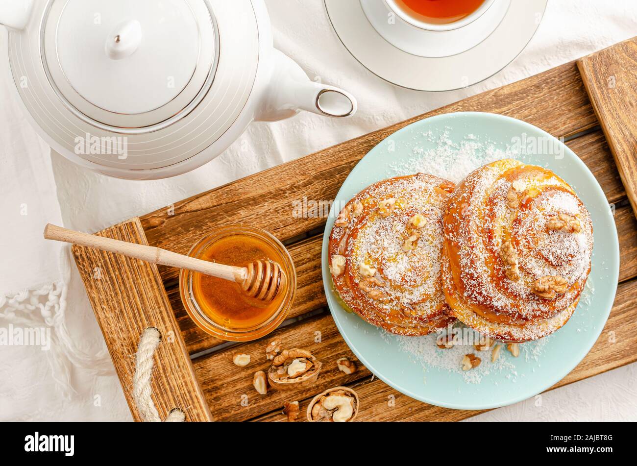 Sweet buns with walnuts, grated coconut and honey on a wooden tray. Breakfast concept. Top view, flat lay. Stock Photo