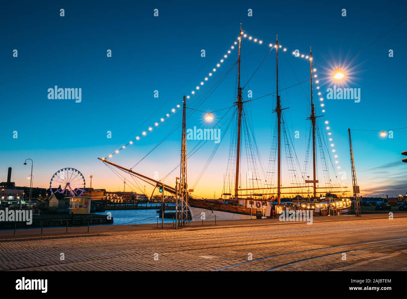 Helsinki, Finland Old Wooden Sailing Vessel Ship Schooner Is Moored To The City Pier, Jetty. Unusual Cafe Restaurant In City Center In Lighting At Eve Stock Photo