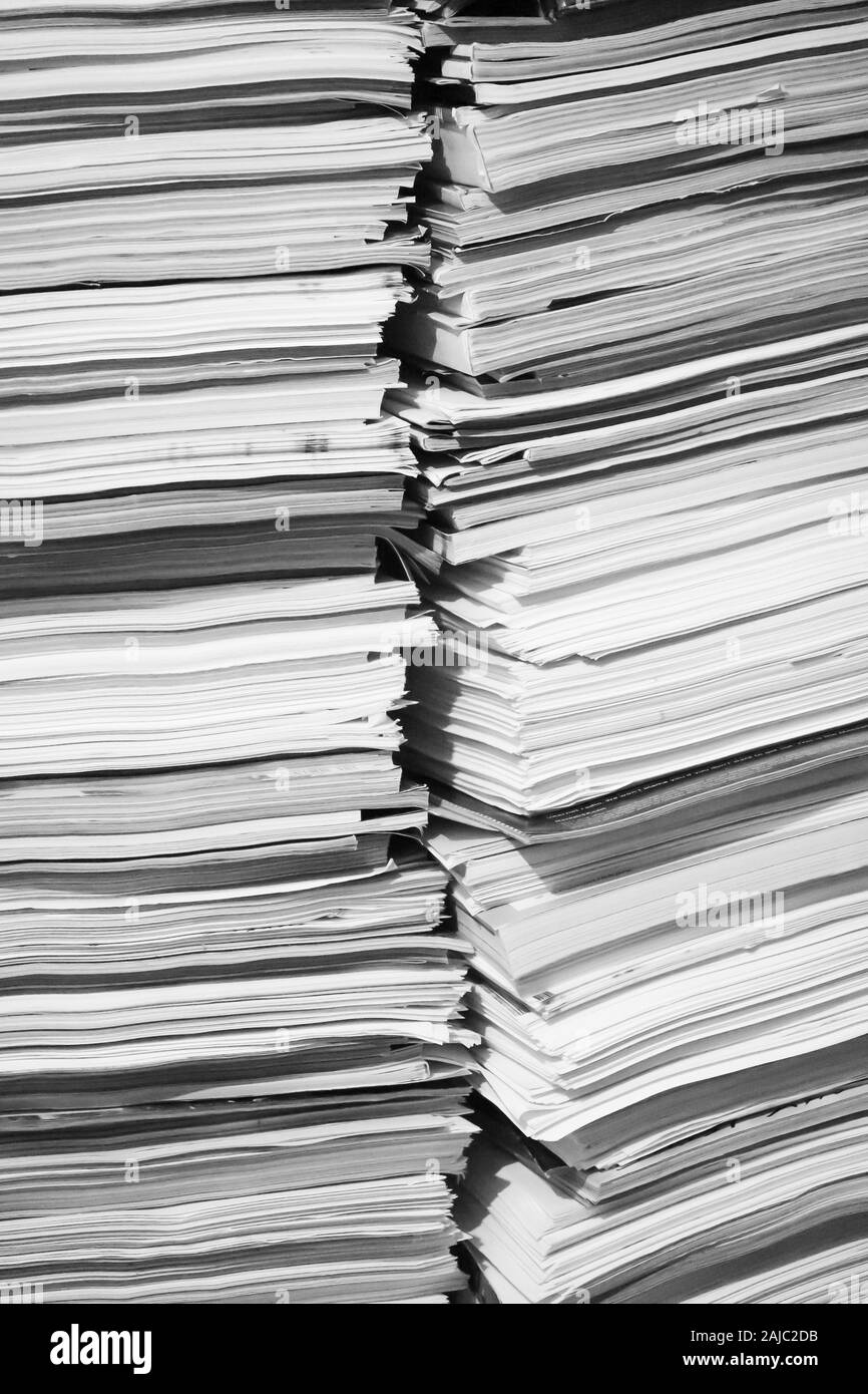 A close-up black-and-white image of a tall pile of papers, documents, and magazines. Stock Photo