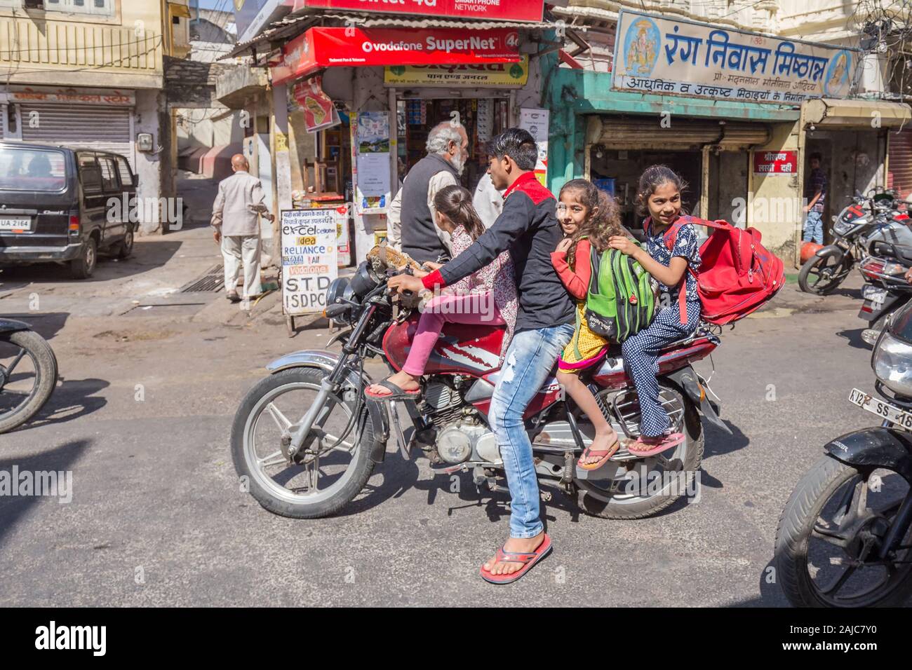 Udaipur, India - March 05 2017: A young guy carries three girls on a motorcycle to school. The girls are smiling and looking funny. Stock Photo