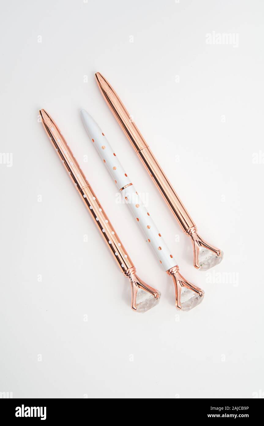 Three designer ball point pens isolated on a light background, set in a diagonal orientation.  Two pens are rose gold color, one is white with polka d Stock Photo