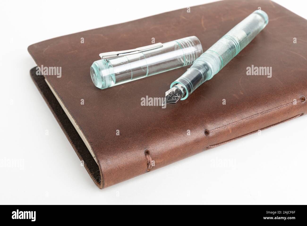 A simple but artful combination of classic leather-bound journal and green glass fountain pen set on a plain white background. Stock Photo