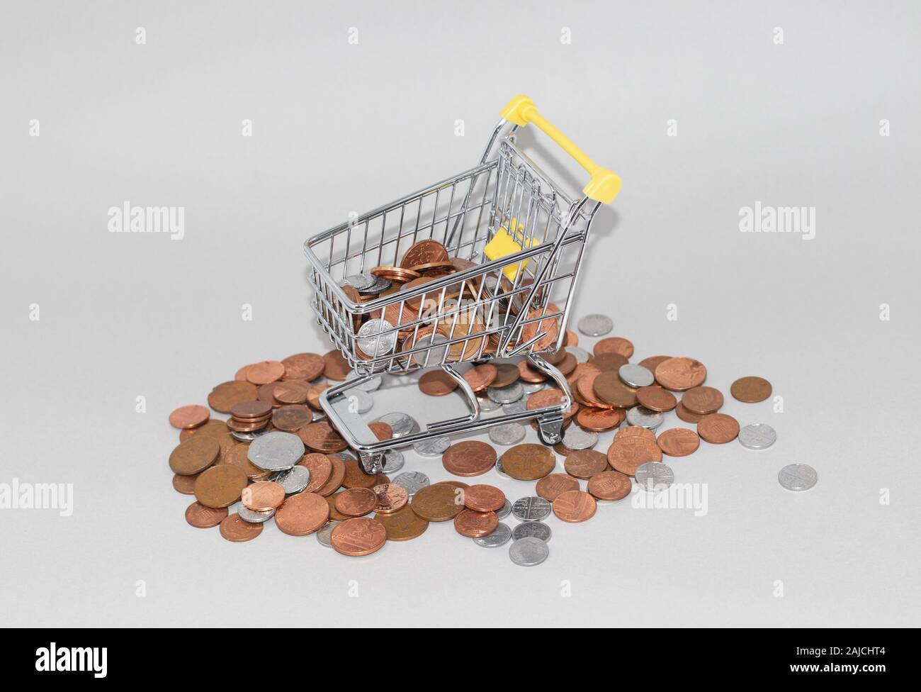 Shopping trolley cart surrounded by loose change, british penny coins. Overspending and cost of living concept Stock Photo