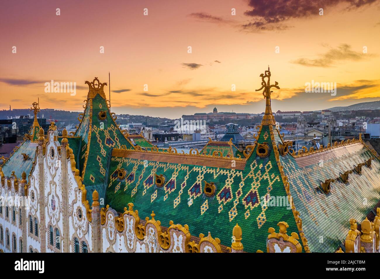 Budapest, Hungary - Aerial view of the colorful rooftop of State Treasury building with Buda Castle Royal Palace and golden sunset at background. Roof Stock Photo