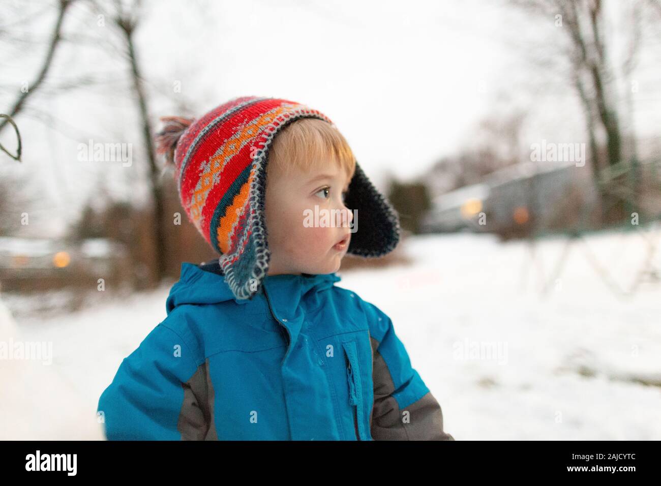Side view portrait of toddler boy wearing knit hat outdoors in snow Stock Photo