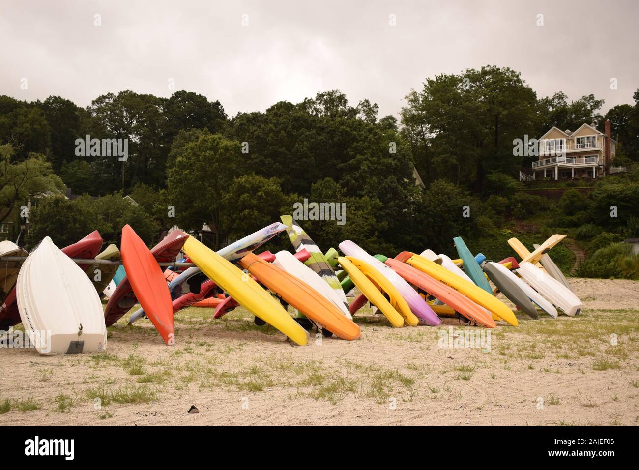 A group of kayak, rowboats and stand up paddleboards lined up on a rack at a rocky beach. Stock Photo