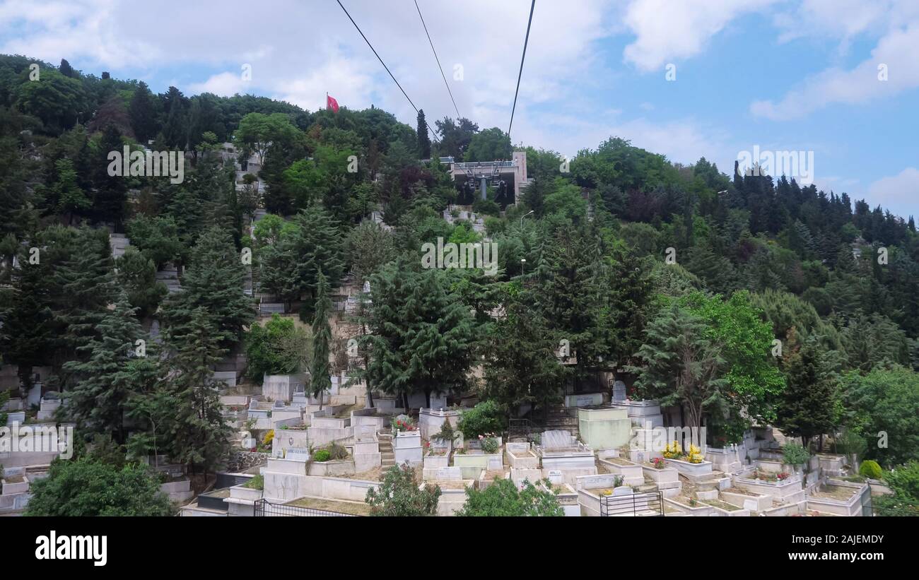 view from moving cableway cabin to traditional Muslim cemetery located on hills among green plants under sky with clouds sky Stock Photo