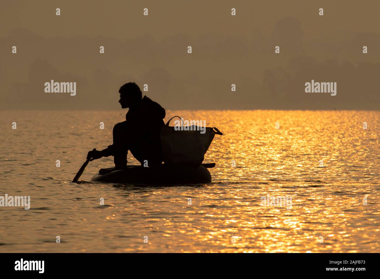 Bichhiya / India / November 29, 2019 - Silhouette photo Indian fisherman is fishing in the pond by sitting in a tube. Stock Photo