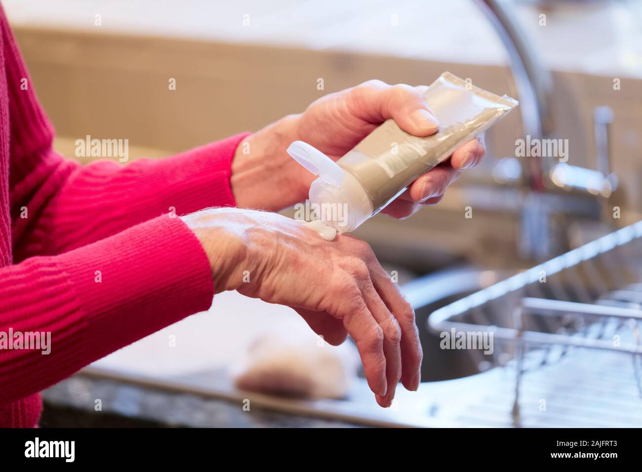 Elderly senior lady applying hand cream to old wrinkled cracked dry hands to moisturise for skin care Stock Photo