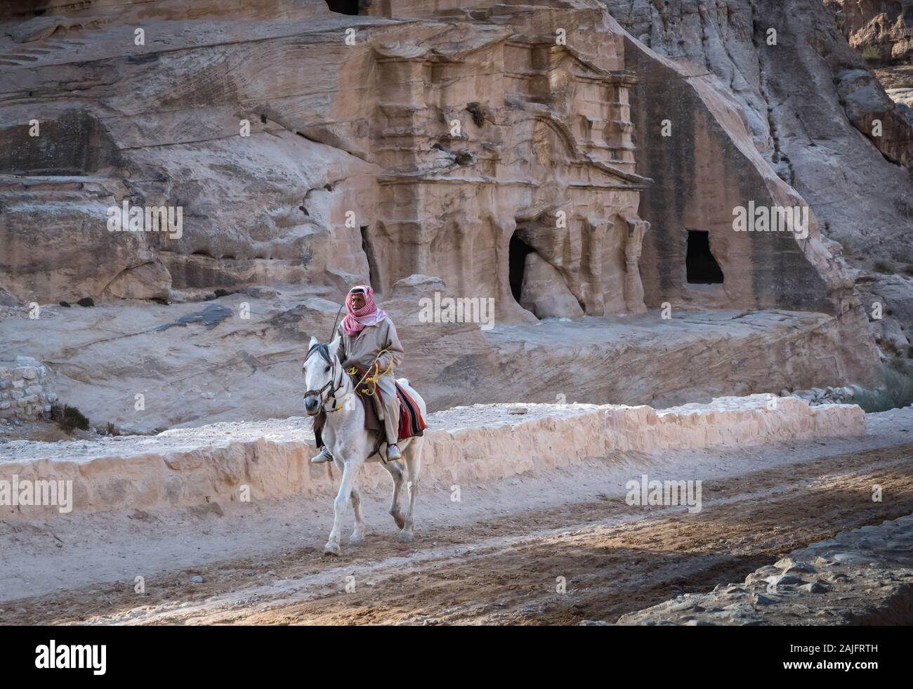 Petra, Jordan: Bedouin man riding a white horse nearby the archaeological area of the Treasury, UNESCO World Heritage Site Stock Photo