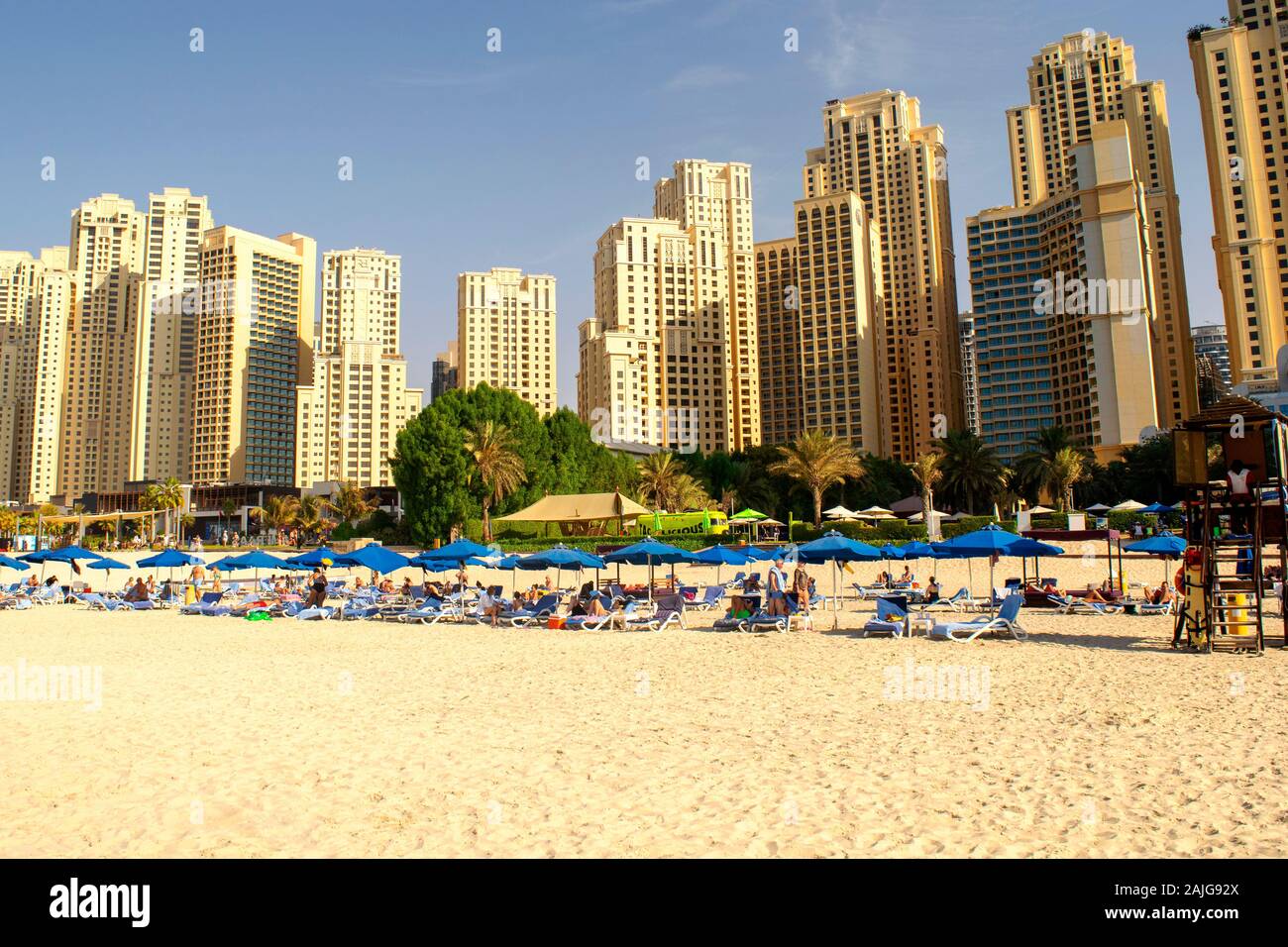 Dubai / UAE - November 7, 2019: JBR. Beautiful view of Jumeirah Beach Residence skyscrapers. Urban beach in the Middle East. Blue sunbeds. Stock Photo