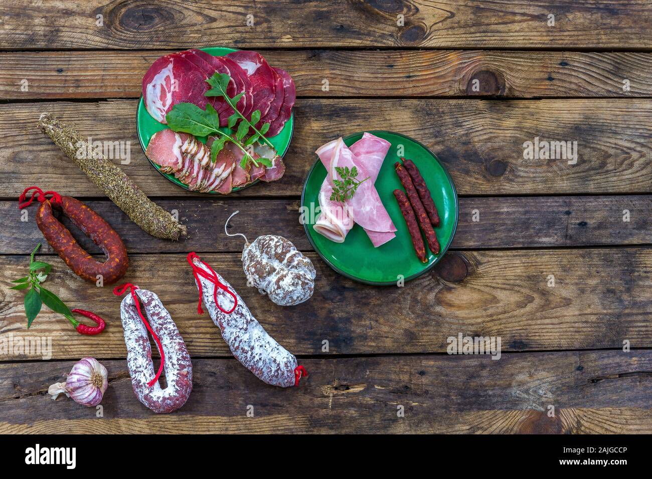 Selection of french raw charcuterie in green plates, with arugula leaves and dry sausage over a wooden background Stock Photo