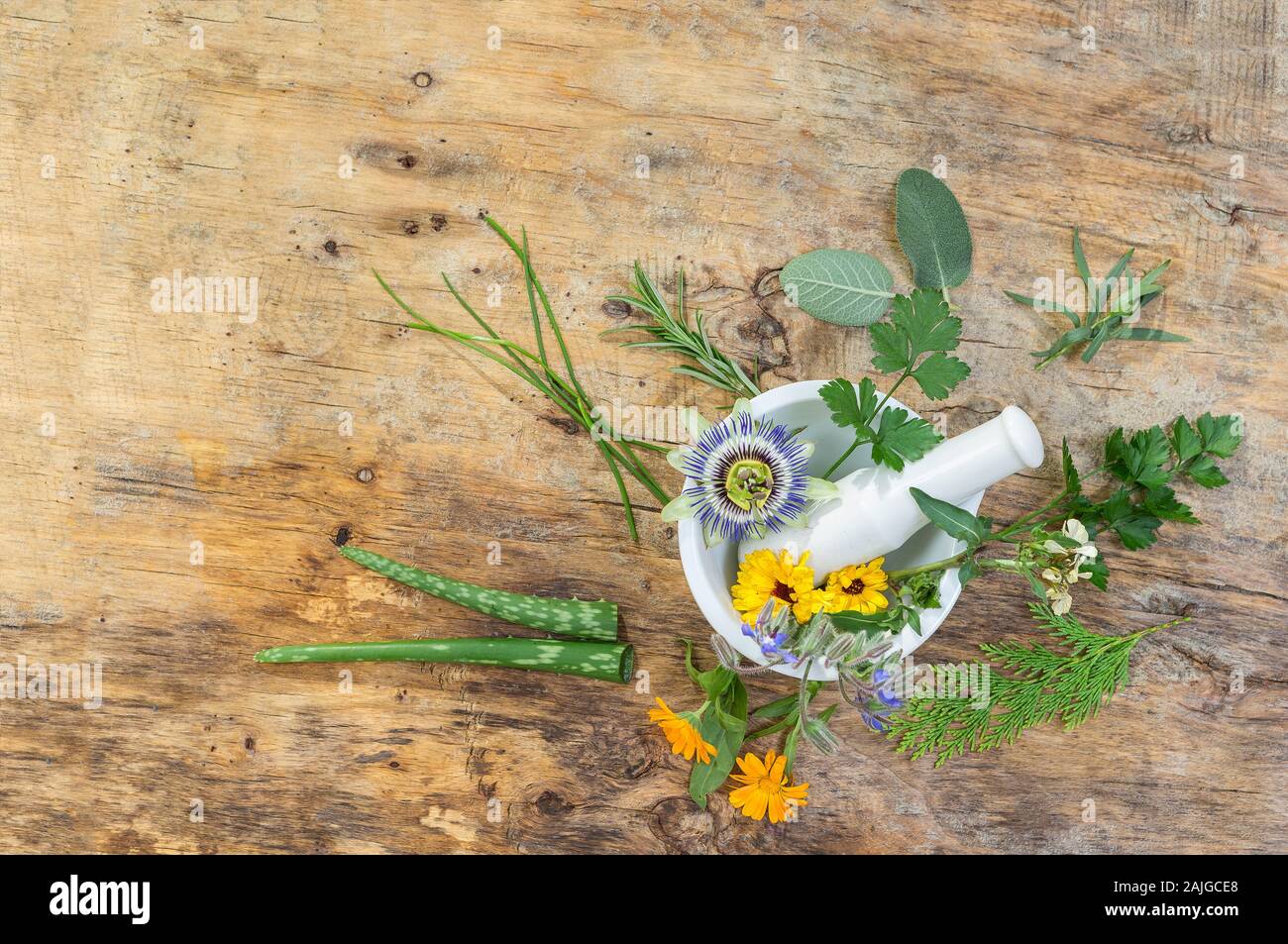 Herb leaf selection of golden thyme, oregano, purple sage, mint and rosemary in flower in a rustic olive wood mortar with pestle, isolated on wooden board background. Stock Photo