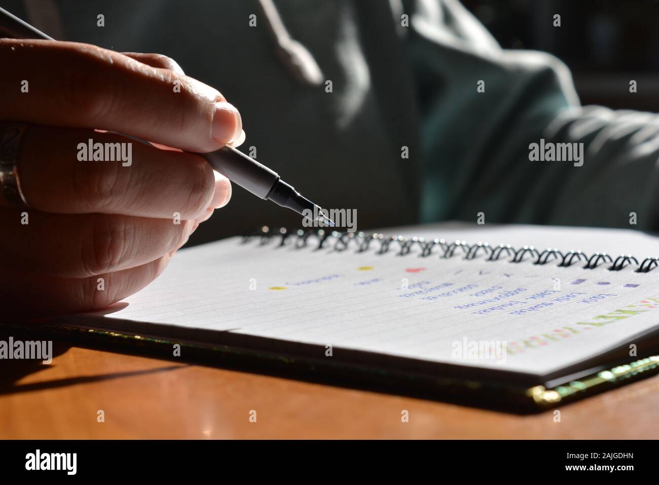Woman writing in a bullet journal, low angle mid section view,  selective focus on pen nib. Stock Photo