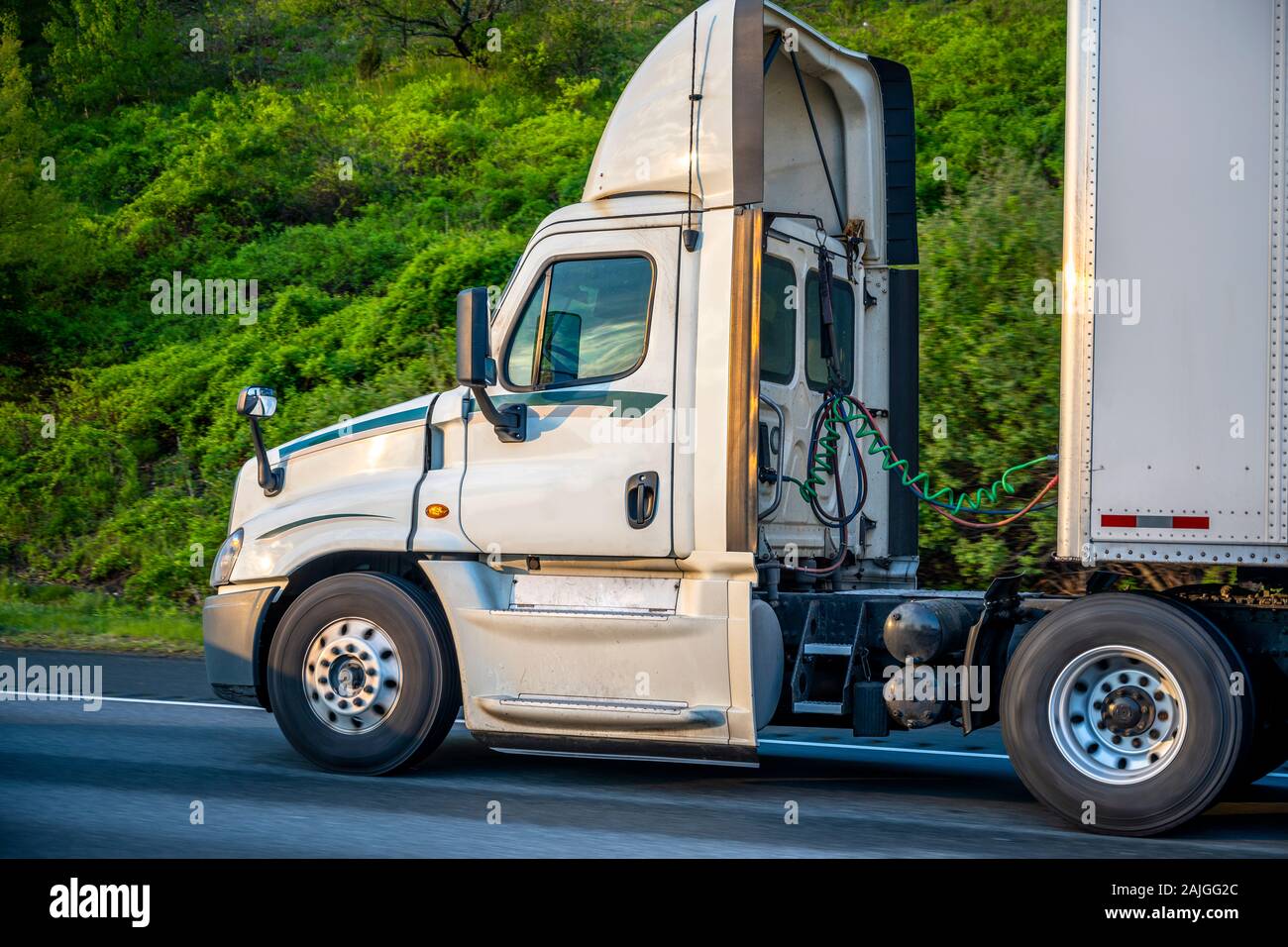 White Big rig day cab semi truck with roof spoiler for better aerodynamics and air resistance improvements transporting cargo in dry van semi trailer Stock Photo