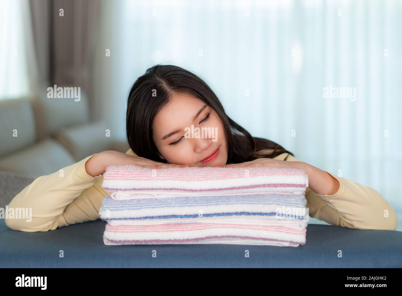Happy Asian woman sleeping on clean folded clothes at home. Pretty young lady sitting in floor with sofa she dreamlike about something. Stock Photo