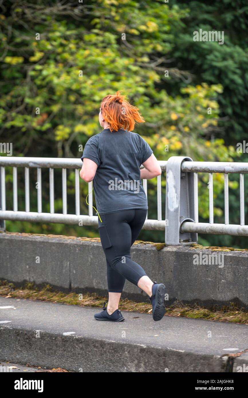 Plus size woman in sportswear engaged in amateur sports for loose weight running on the city street preferring an active lifestyle to maintain health Stock Photo