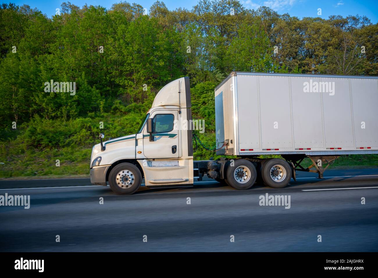 White Big rig day cab semi truck with roof spoiler for better aerodynamics and air resistance improvements transporting cargo in dry van semi trailer Stock Photo