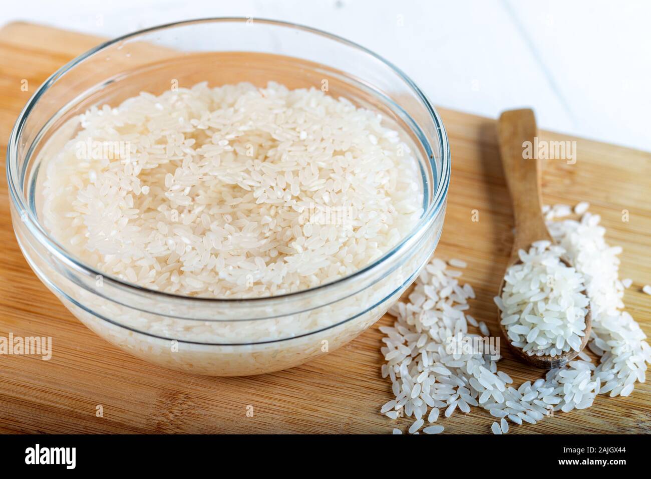 Soaked rice, grain, cloudy liquid water in glass bowl on wooden