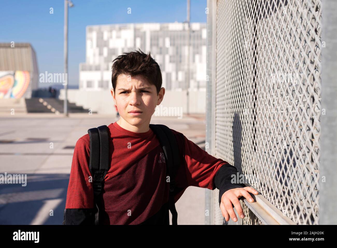 Portrait of cheerful teen leaning on metallic fence while looking away Stock Photo