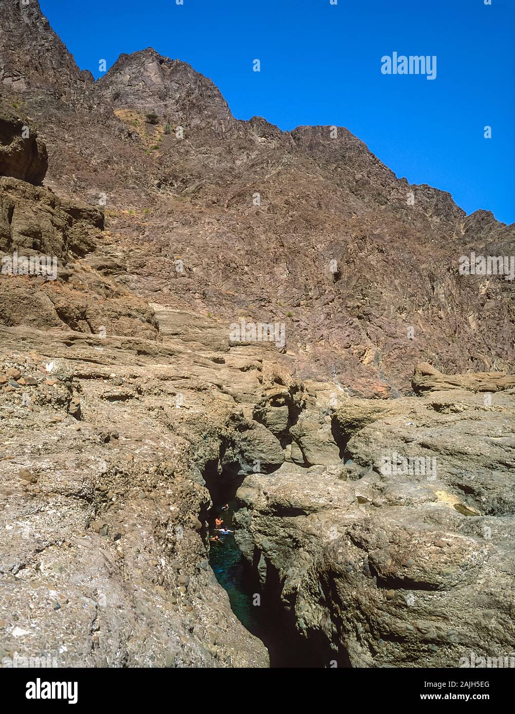 Tourists enjoy a swim at Hatta Pools in the rugged scenery of the Al Hajr and Musandan mountains of the Arabian Peninsula shared by the Emirates of Dubai, Ras Al Khaimah and Fujairah, seen here in Springtime Stock Photo