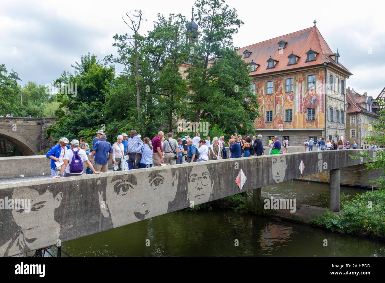 People walking across the Untere Brücke with faces on the side in Bamberg, Upper Franconia, Bavaria, Germany. Stock Photo