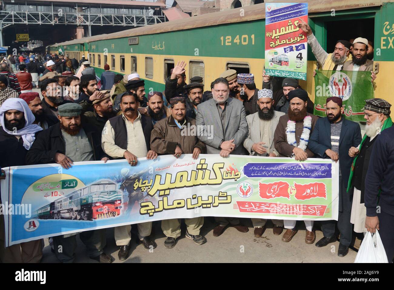 Activists of Pakistan Sunni Tahreek (PST) holding party flag while installed banner on train during their departure titled “Jalta Kashmir Bachao Train March” from Lahore to Karachi at Railway Station in provincial capital Lahore. Pakistan Sunni Tahreek (PST) titled “Jalta Kashmir Bachao Train March” from Lahore to Karachi express solidarity with the people of Indian occupied Kashmir (IOK) who have been living under curfew imposed by the Indian government on August 5, 2019.Central leader of Pakistan Sunni Tahreek (PST) Shahdab Raza Nakshbandi, Dr Shahid Hussain, Sharif-u-ddin Qaddafi, Sardar Ta Stock Photo