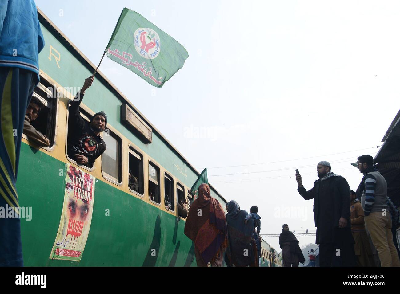 Activists of Pakistan Sunni Tahreek (PST) holding party flag while installed banner on train during their departure titled “Jalta Kashmir Bachao Train March” from Lahore to Karachi at Railway Station in provincial capital Lahore. Pakistan Sunni Tahreek (PST) titled “Jalta Kashmir Bachao Train March” from Lahore to Karachi express solidarity with the people of Indian occupied Kashmir (IOK) who have been living under curfew imposed by the Indian government on August 5, 2019.Central leader of Pakistan Sunni Tahreek (PST) Shahdab Raza Nakshbandi, Dr Shahid Hussain, Sharif-u-ddin Qaddafi, Sardar Ta Stock Photo