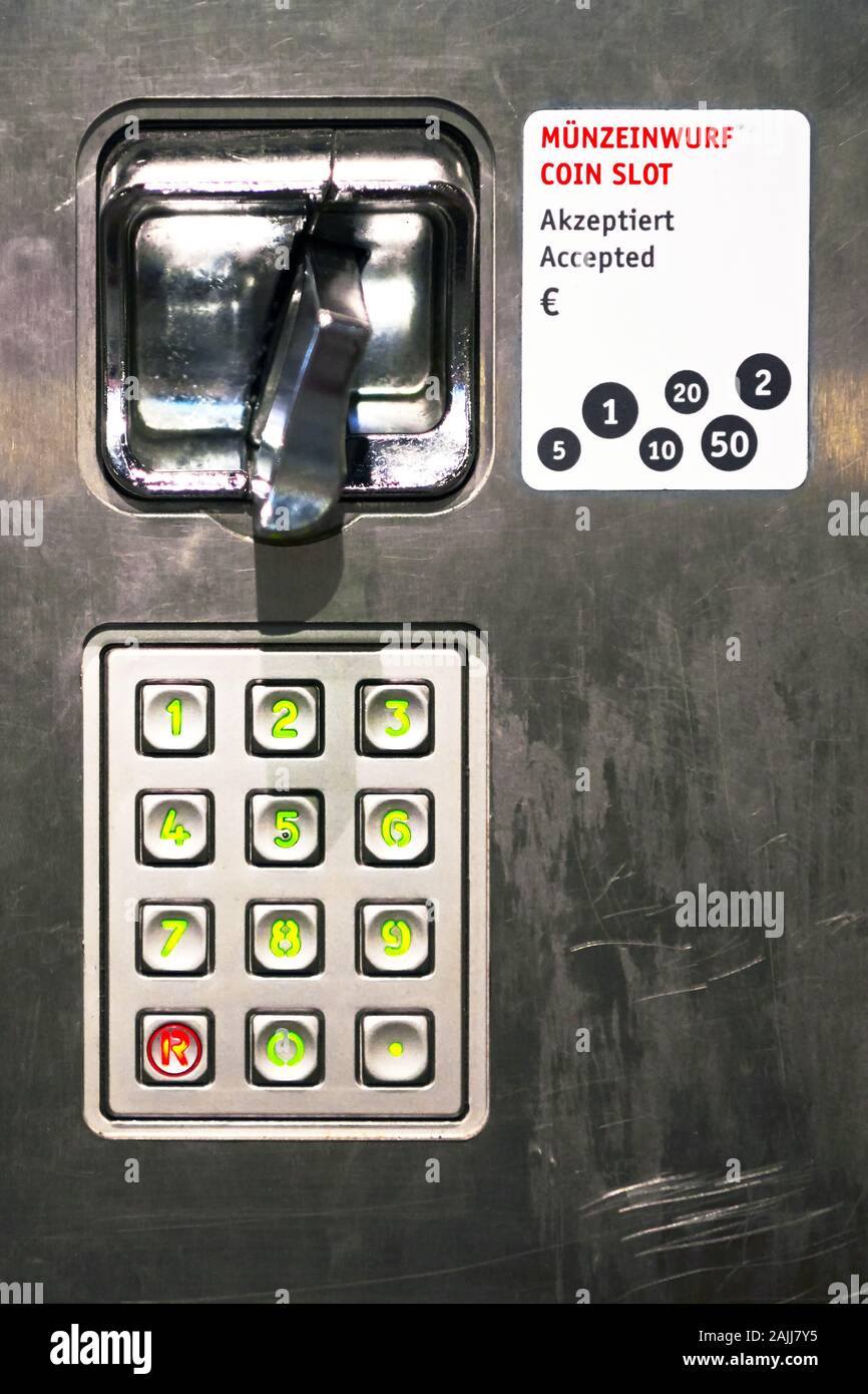 Close-up detail view of a metal pay phone coin slot and a keypad with green illuminated numbers, seen at a train station in Germany Stock Photo