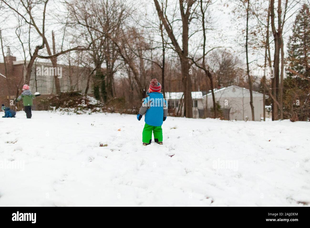 Three children in cold weather gear play in backyard after a snowstorm Stock Photo