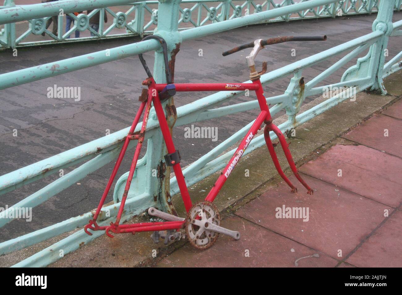 Red bike frame, abandoned, padlocked to railing, missing wheels and peddles, vandalised, no chain Stock Photo