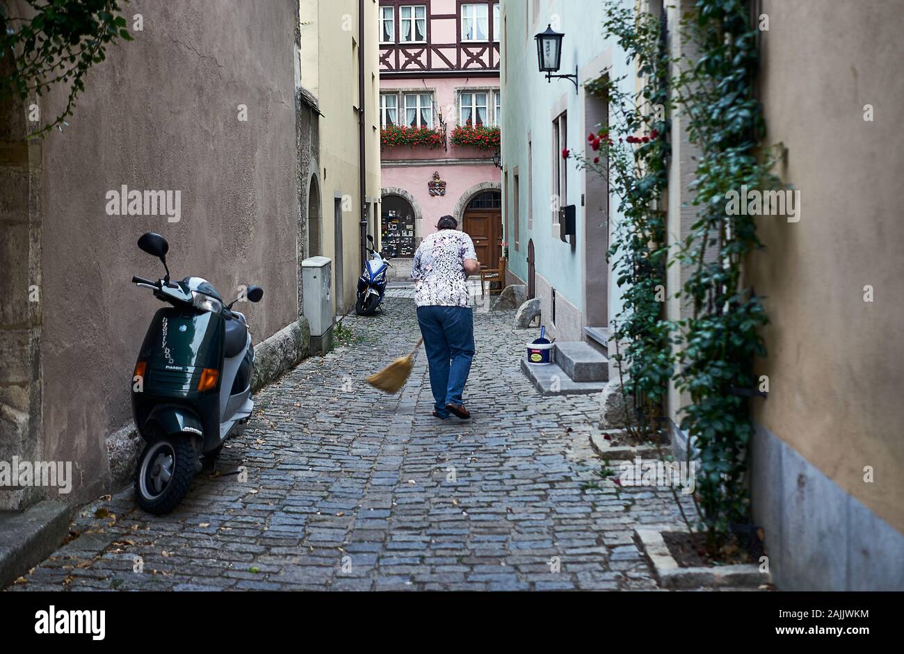 Typical German street scene with woman taking a broom to the cobblestones outside her house on a narrow land in Rothenburg, Germany. Stock Photo