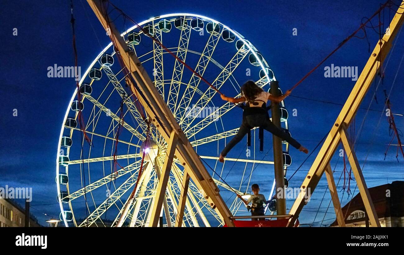 Kids bungee jumping next to a large ferris wheel at a summer festival