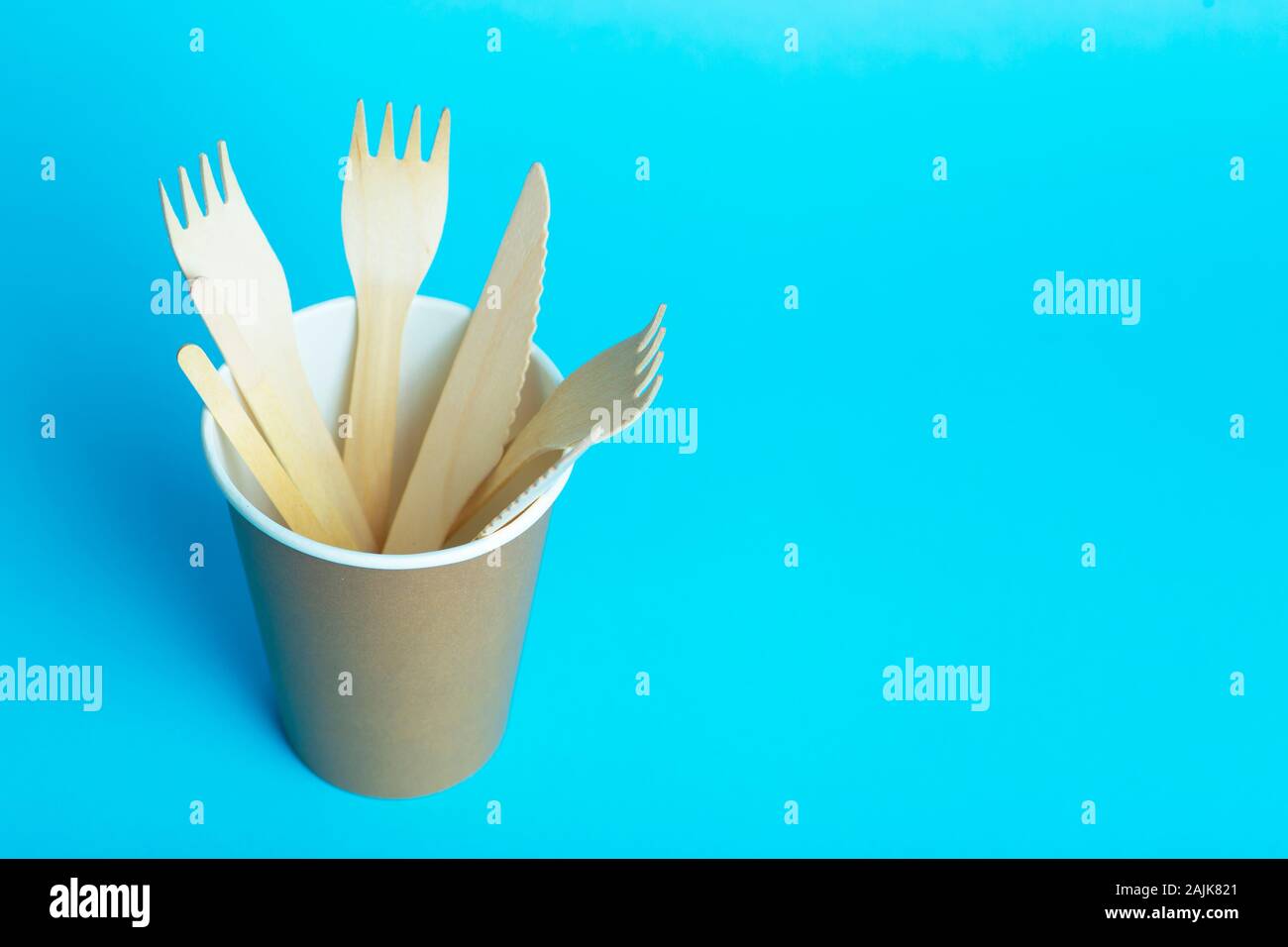 Wooden forks, knives and spoons for food in a paper cup on a colored ...