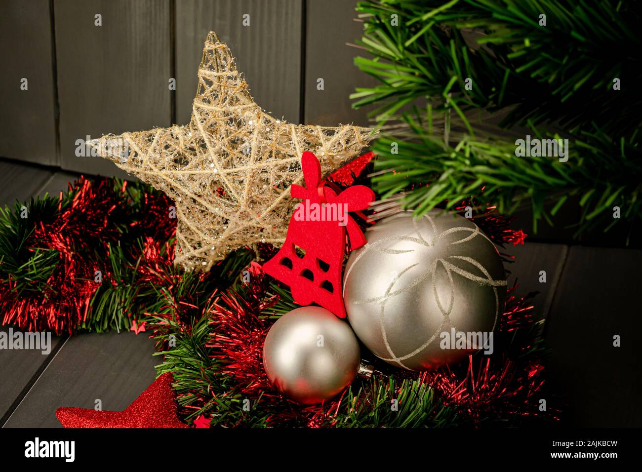 Christmas decoration with silver balls, green and red tinsel, red and gold stars, velvet bell and Christmas tree on dark wooden background Stock Photo