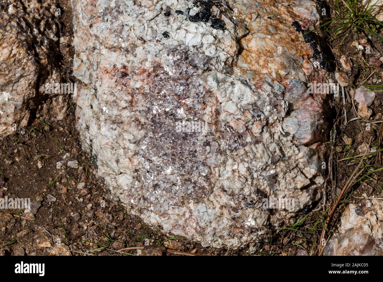 A large rock embedded in the ground that is a composition of quartz crystal, granite, and mica that sparkles in the sunshine. Stock Photo