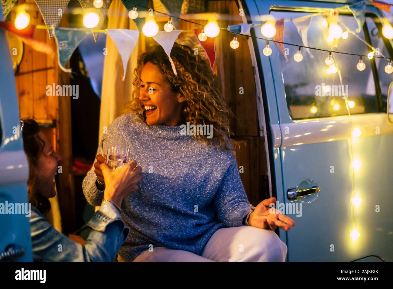 Alternative travel and celebration concept with couple of people adult cheerful happy women celebrate together in a vintage van camper  and party ligh Stock Photo
