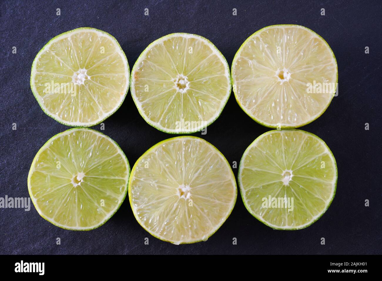 Six juicy lime halves on a black slate background; landscape view Stock Photo