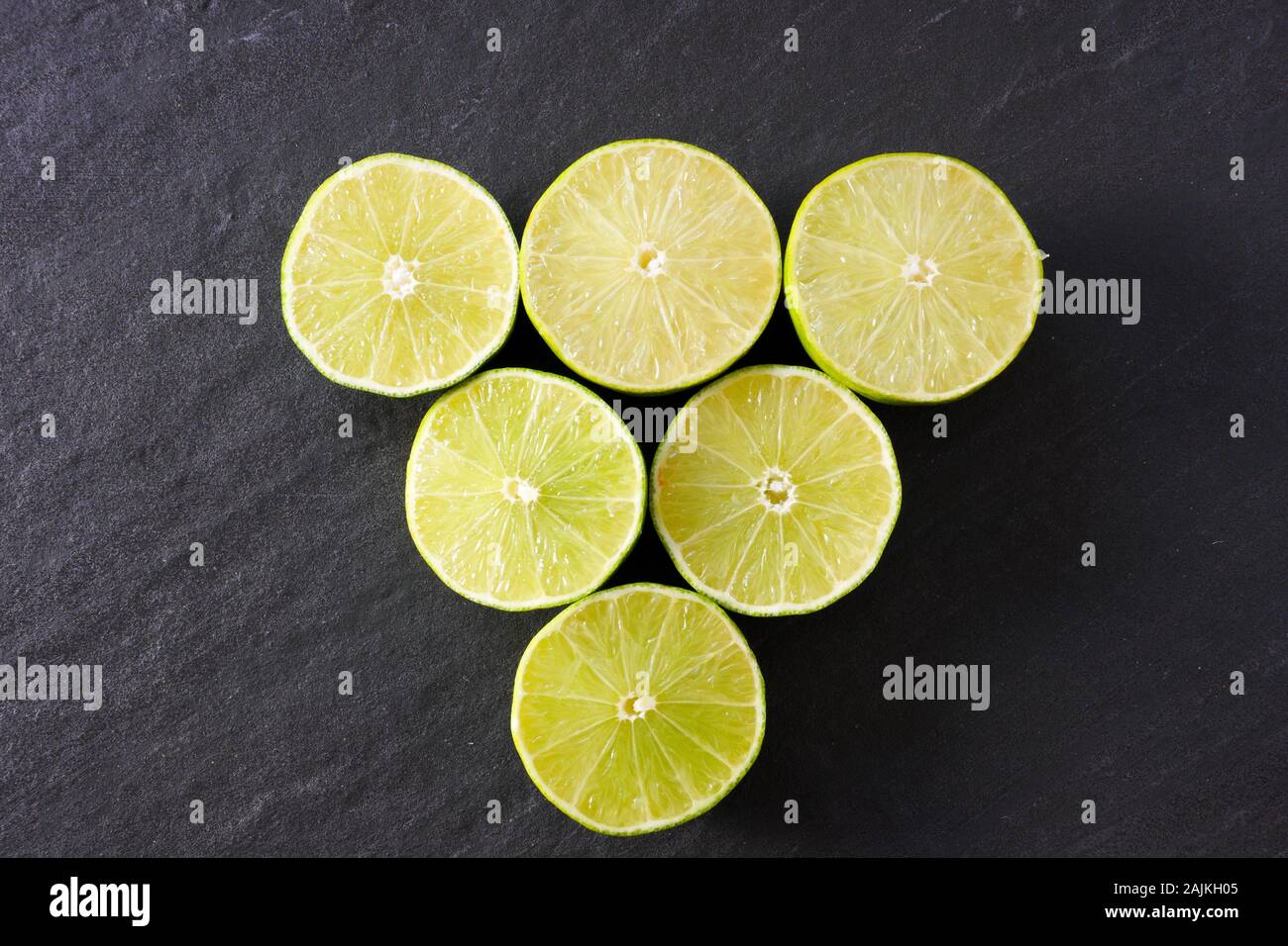 A triangle of lime halves  on a black slate background with copy space; landscape view Stock Photo