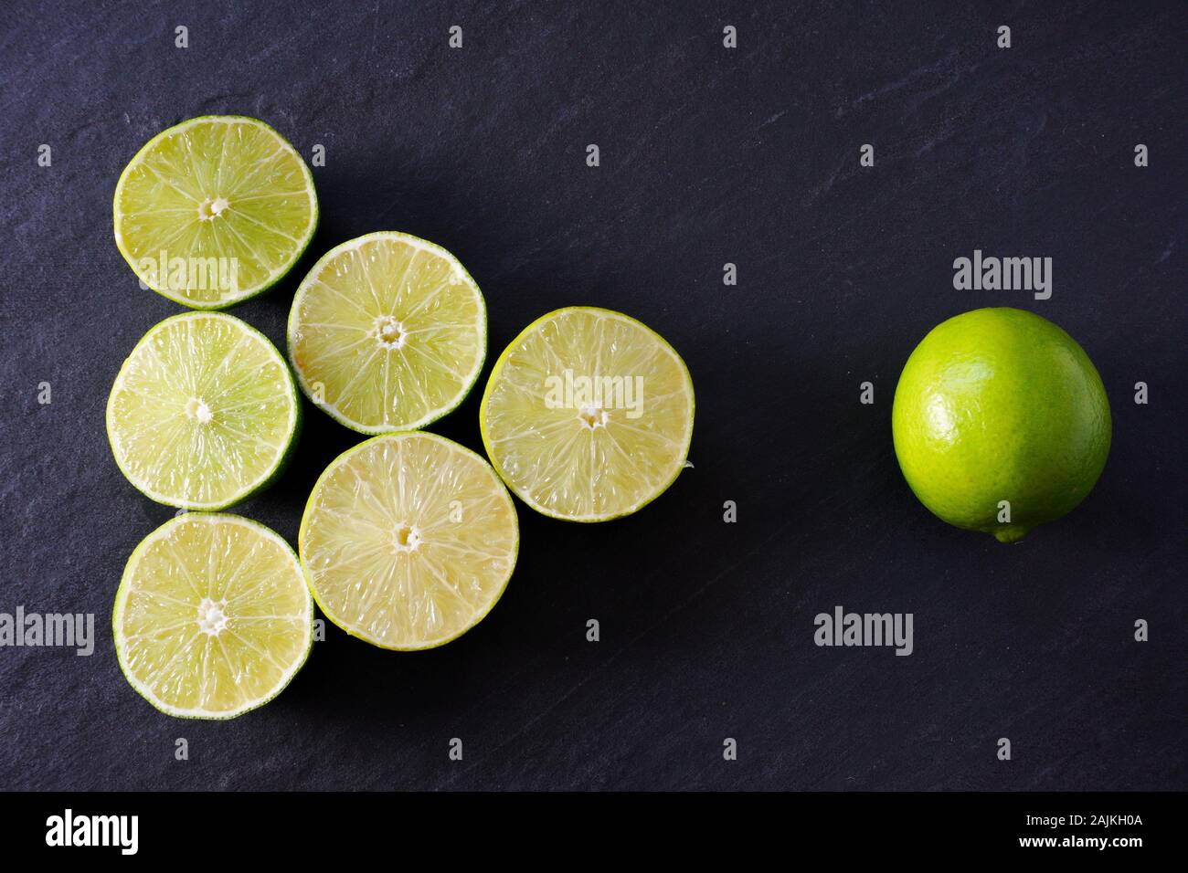 A triangle of lime halves point to a whole lime on a background of black slate; copy space Stock Photo